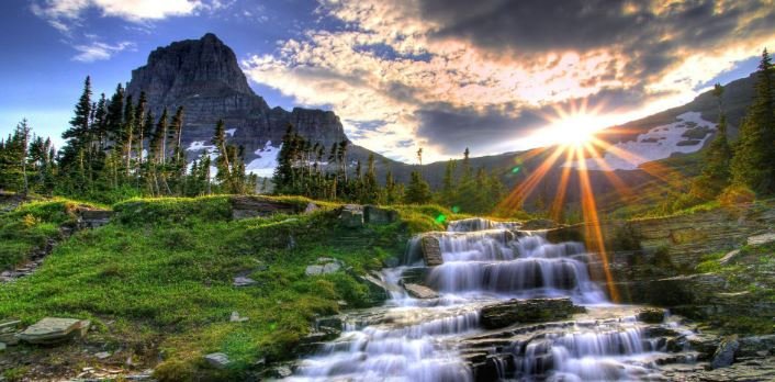 A serene mountain waterfall glistens under the bright sun, surrounded by lush greenery and rocky terrain