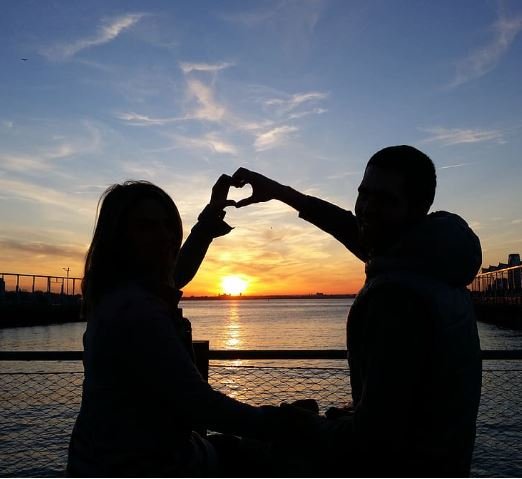 A couple forms a heart shape with their hands, symbolizing love and connection in a warm, intimate moment.