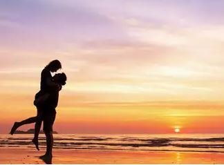 A couple's silhouette on the beach at sunset, framed by vibrant colors of the sky, symbolizing love and serenity.