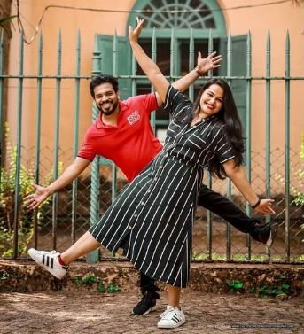 A happy couple poses for a picture, framed by a contemporary building with a sleek design and vibrant surroundings.