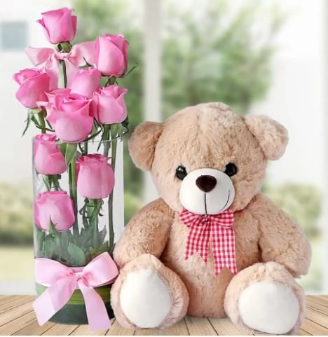 A teddy bear nestled beside a vase filled with vibrant pink roses, creating a charming and affectionate display.