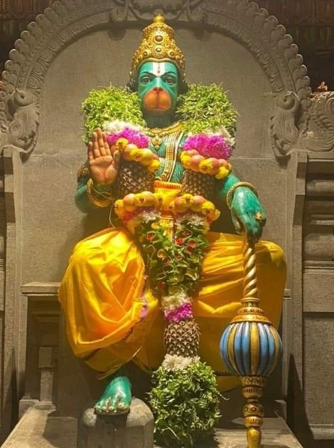 A statue of Hanuman adorned with flowers, situated within a serene temple setting, symbolizing devotion and spirituality.