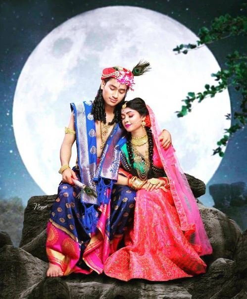 A couple in vibrant traditional Indian clothing sits on a rock, exuding elegance amidst a picturesque outdoor setting.
