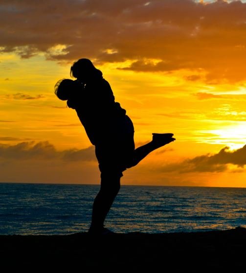 A man and woman are silhouetted against a vibrant sunset, creating a romantic and serene atmosphere.