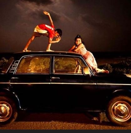 Two people standing on a car in a dimly lit environment, capturing a moment of camaraderie and thrill in the nigh